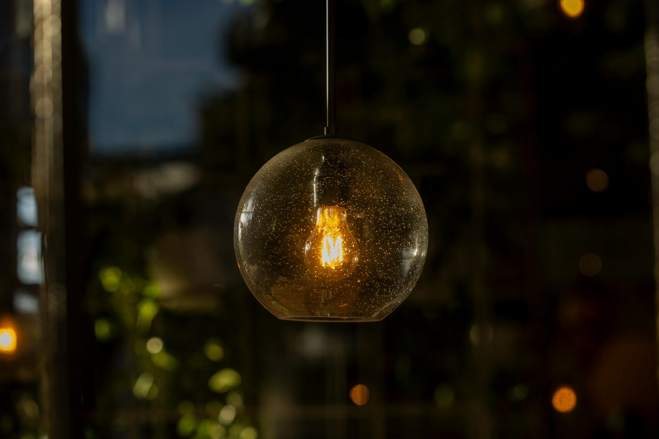 Capture of a glowing vintage-style glass pendant light indoors at night.